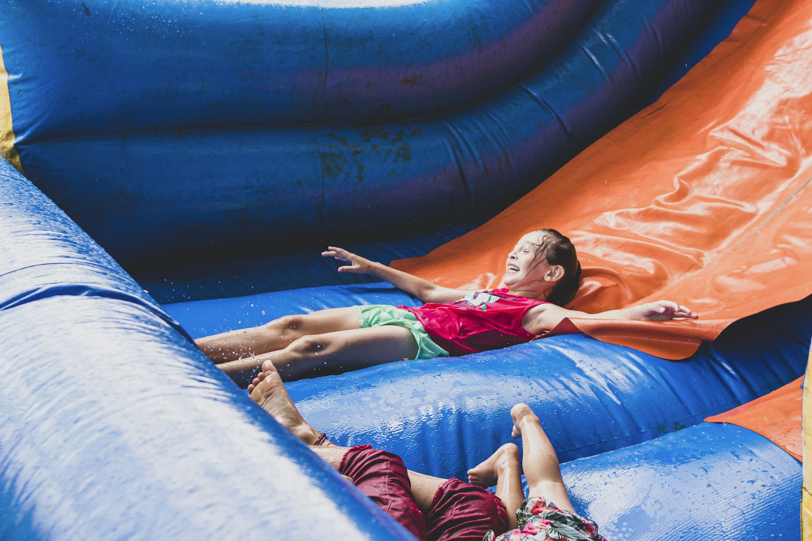 A young girl laughing while lying on a wet inflatable slide.