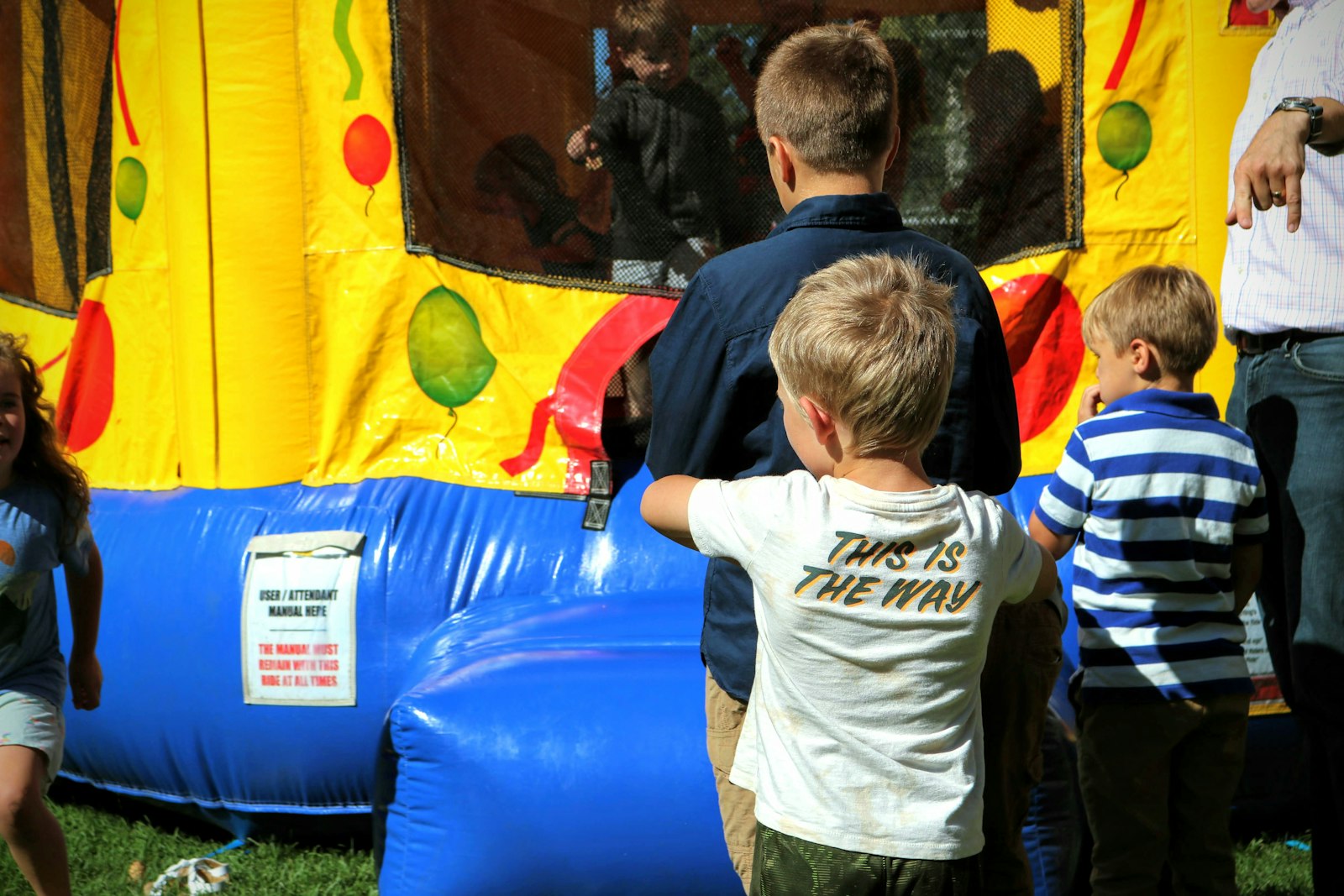 Children standing in front of a colorful inflatable bounce house at an outdoor event.