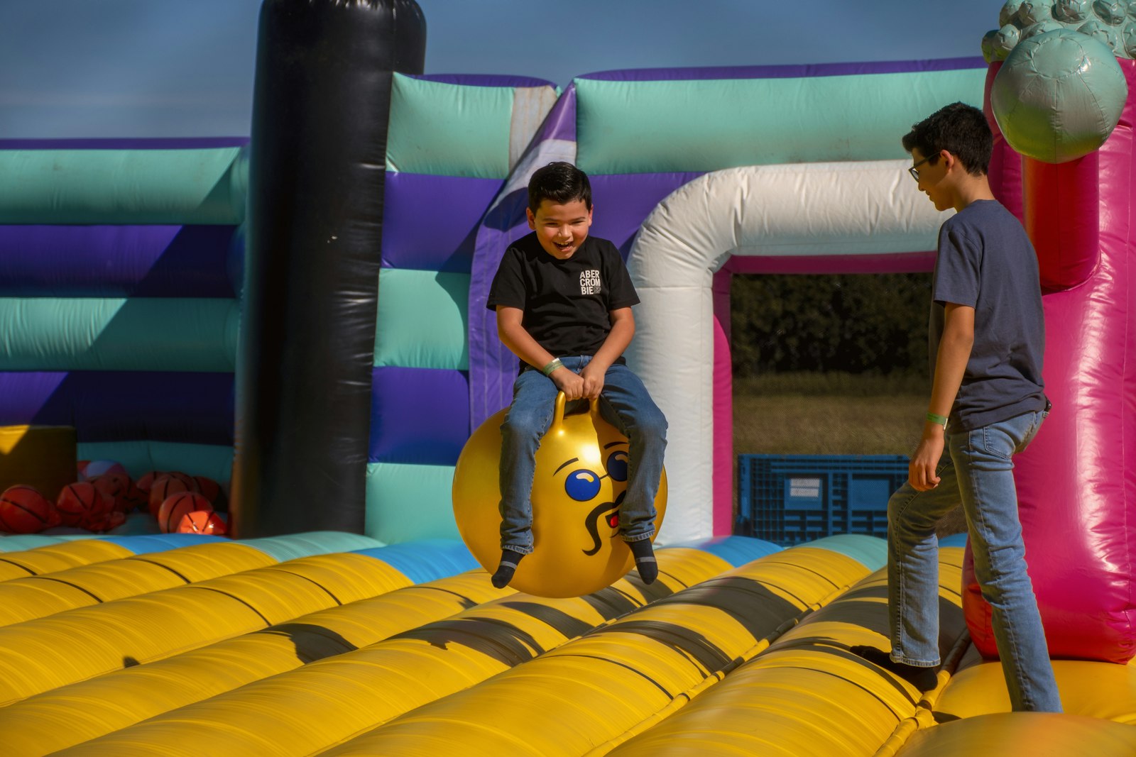 A boy bouncing on a yellow inflatable ball inside a bounce house.