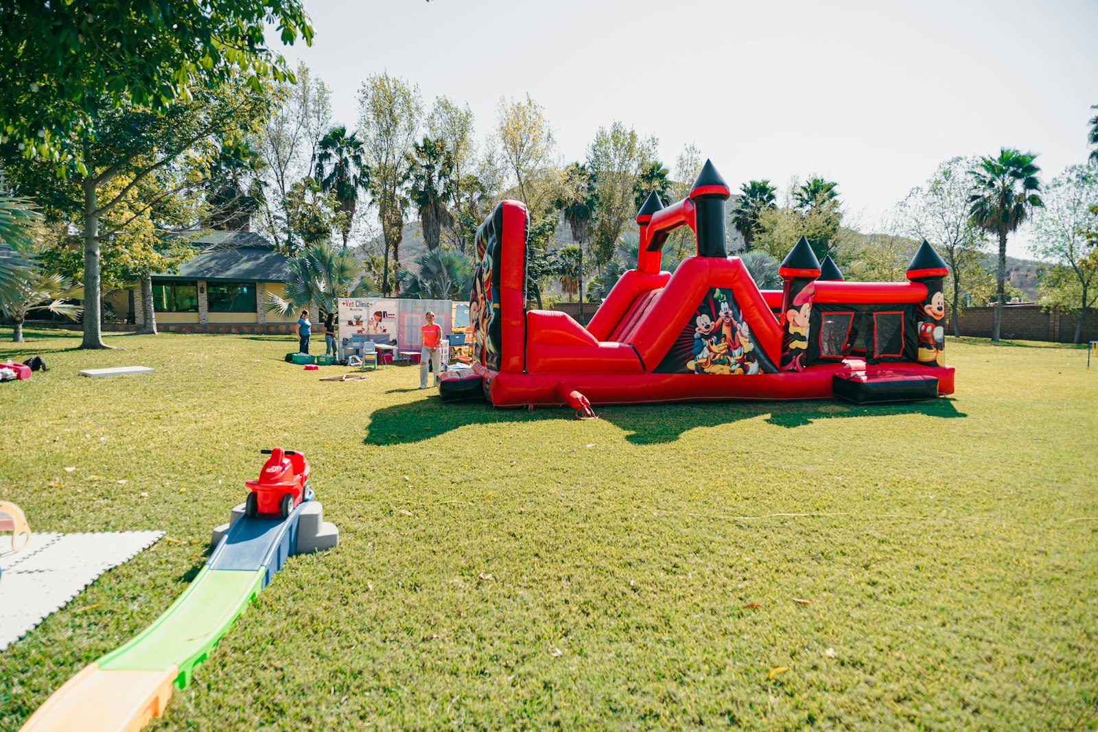A large red inflatable bounce house set up on a grassy field with a small toy track in the foreground.
